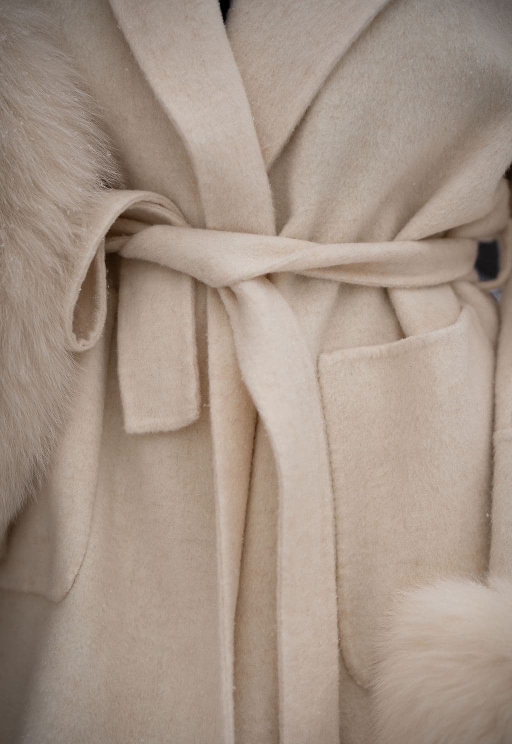 The wool body and self-tie belt of an ivory coat, with fox at the cuff.