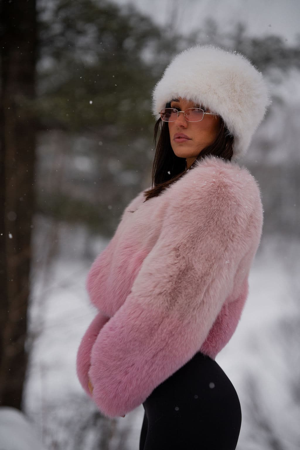 A blush fox jacket and a white fur hat, seen in profile in falling snow.