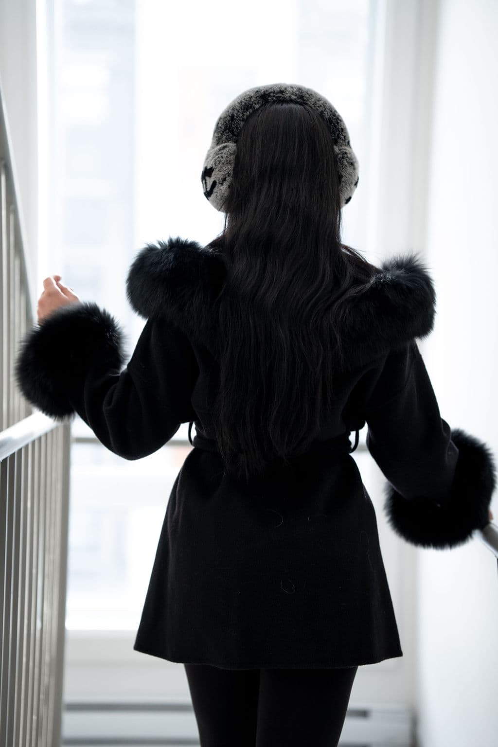 A black wool coat seen from behind, belted, with fox at the hood and cuffs.